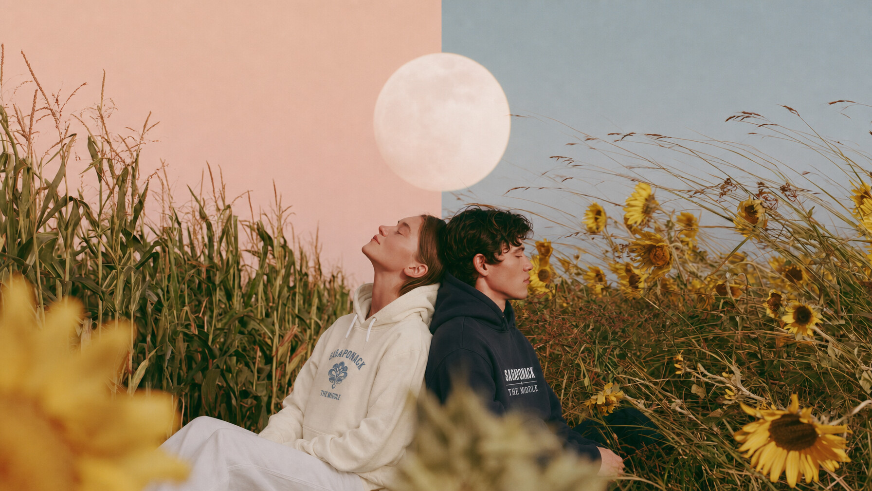 Two figures in Sagaponack sweatshirts sitting back to back between a cornfield and sunflowers, beneath a full moon